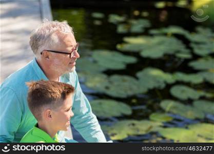 family, generation, communication and people concept - happy grandfather and grandson sitting on river berth
