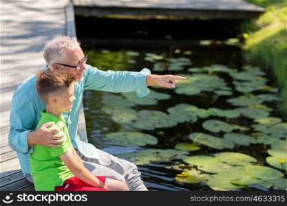 family, generation, communication and people concept - happy grandfather and grandson sitting on river berth