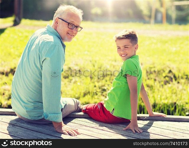family, generation, communication and people concept - happy grandfather and grandson sitting on river berth. grandfather and grandson sitting on river berth