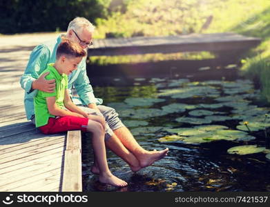 family, generation, communication and people concept - happy grandfather and grandson sitting on river berth. grandfather and grandson sitting on river berth