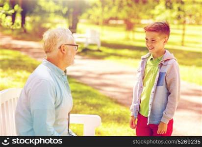 family, generation, communication and people concept - happy grandfather and grandson talking at summer park. grandfather and grandson talking at summer park