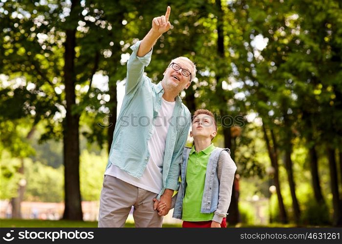 family, generation, communication and people concept - happy grandfather and grandson walking and pointing fingers up at summer park