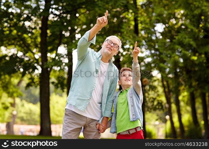 family, generation, communication and people concept - happy grandfather and grandson walking and pointing fingers up at summer park
