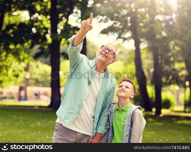 family, generation, communication and people concept - happy grandfather and grandson walking and pointing fingers up at summer park. grandfather and boy pointing up at summer park