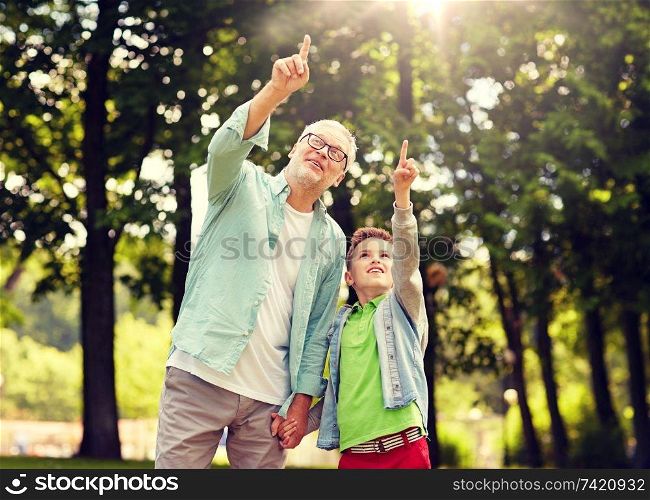 family, generation, communication and people concept - happy grandfather and grandson walking and pointing fingers up at summer park. grandfather and boy pointing up at summer park