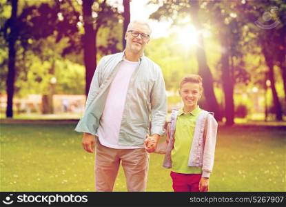 family, generation, communication and people concept - happy grandfather and grandson walking at summer park. grandfather and grandson walking at summer park
