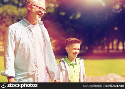 family, generation, communication and people concept - happy grandfather and grandson walking at summer park. grandfather and grandson walking at summer park