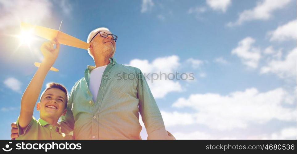 family, generation, future, dream and people concept - happy grandfather and grandson with toy airplane over blue sky and clouds background