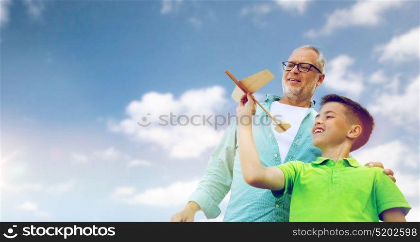 family, generation, future, dream and people concept - happy grandfather and grandson with toy airplane over blue sky. senior man and boy with toy airplane over sky