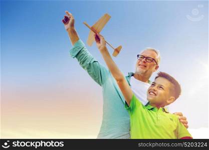 family, generation, future, dream and people concept - happy grandfather and grandson with toy airplane over blue sky. senior man and boy with toy airplane over sky