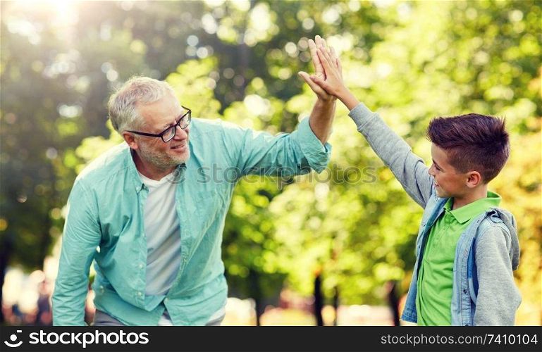 family, generation, gesture and people concept - happy grandfather and grandson making high five at summer park. old man and boy making high five at summer park