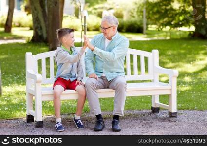 family, generation, gesture, communication and people concept - happy grandfather and grandson making high five on bench at summer park