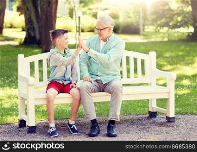 family, generation, gesture, communication and people concept - happy grandfather and grandson making high five on bench at summer park. old man and boy making high five at summer park