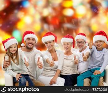 family, generation, gesture, holidays and people concept - happy family in santa helper hats showing thumbs up over red lights background