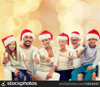 family, generation, gesture, holidays and people concept - happy family in santa helper hats showing thumbs up over beige lights background