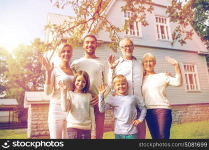 family, generation, gesture, home and people concept - happy family standing in front of house waving hands outdoors. happy family in front of house outdoors