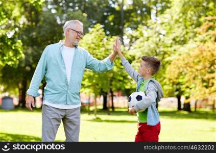 family, generation, gesture, sport and people concept - happy grandfather and grandson with football ball making high five at at summer park