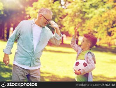 family, generation, gesture, sport and people concept - happy grandfather and grandson with football ball making high five at at summer park. old man and boy with soccer ball making high five