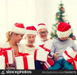 family, generation, holidays and people concept - happy family in santa helper hats with gift boxes sitting over living room with christmas tree background