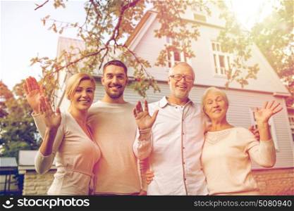 family, generation, home, gesture and people concept - happy family standing in front of house waving hands outdoors. happy family in front of house outdoors