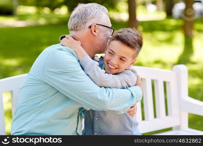 family, generation, relations and people concept - happy grandfather and grandson hugging on bench at summer park