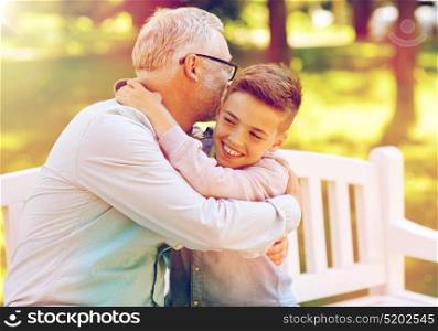 family, generation, relations and people concept - happy grandfather and grandson hugging on bench at summer park. grandfather and grandson hugging at summer park