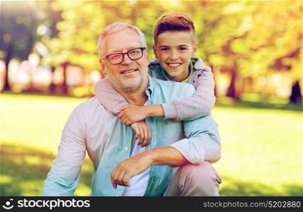 family, generation, relations and people concept - happy grandfather and grandson hugging at summer park. grandfather and grandson hugging at summer park