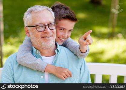 family, generation, relations and people concept - happy grandfather and grandson pointing finger to something at summer park