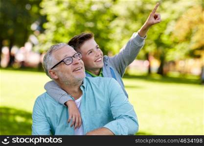 family, generation, relations and people concept - happy grandfather and grandson pointing finger up to something at summer park