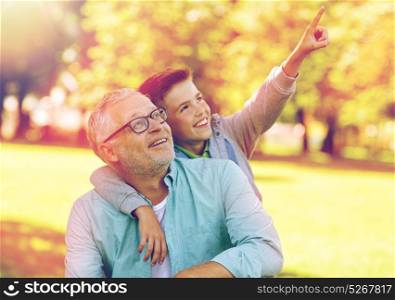 family, generation, relations and people concept - happy grandfather and grandson pointing finger up to something at summer park. grandfather and boy pointing finger at summer park