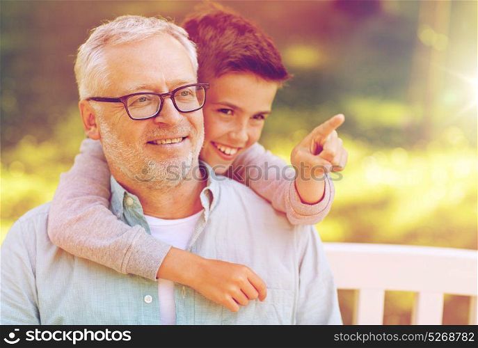 family, generation, relations and people concept - happy grandfather and grandson pointing finger to something at summer park. grandfather and boy pointing finger at summer park