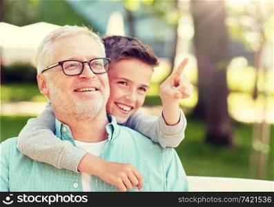 family, generation, relations and people concept - happy grandfather and grandson pointing finger to something at summer park. grandfather and boy pointing finger at summer park