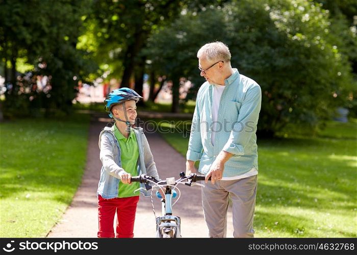 family, generation, safety and people concept - happy grandfather and boy with bicycle and bike helmet talking at summer park