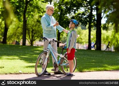 family, generation, safety and people concept - happy grandfather and boy with bicycle and bike helmet at summer park