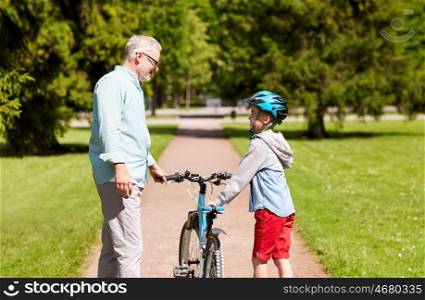 family, generation, safety and people concept - happy grandfather and boy with bicycle and bike helmet talking at summer park