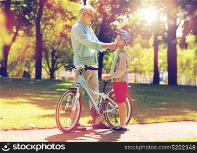 family, generation, safety and people concept - happy grandfather and boy with bicycle and bike helmet at summer park. grandfather and boy with bicycle at summer park