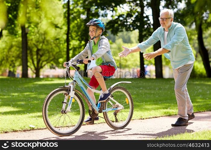 family, generation, safety and people concept - happy grandfather teaching boy how to ride bicycle at summer park