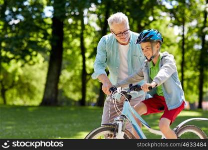family, generation, safety and people concept - happy grandfather teaching boy how to ride bicycle at summer park