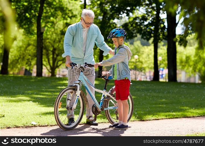 family, generation, safety and people concept - happy grandfather teaching boy with bicycle and bike helmet at summer park