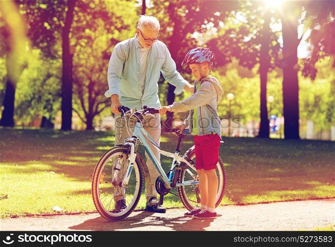 family, generation, safety and people concept - happy grandfather teaching boy with bicycle and bike helmet at summer park. grandfather and boy with bicycle at summer park