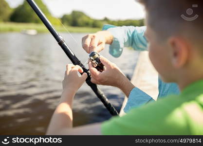 family, generation, summer holidays and people concept - boy and grandfather with fishing rod or spinning on river or lake berth. boy and grandfather with fishing rod on river