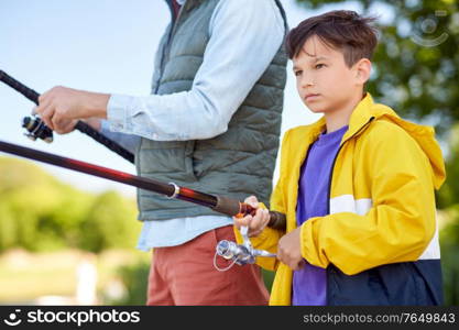 family, generation, summer holidays and people concept - father and son with fishing rods on river berth. father and son fishing on river