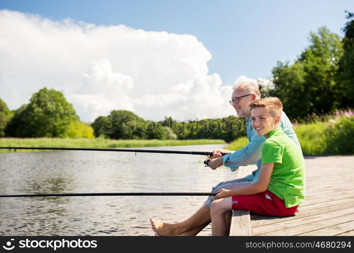 family, generation, summer holidays and people concept - happy grandfather and grandson with fishing rods on river berth