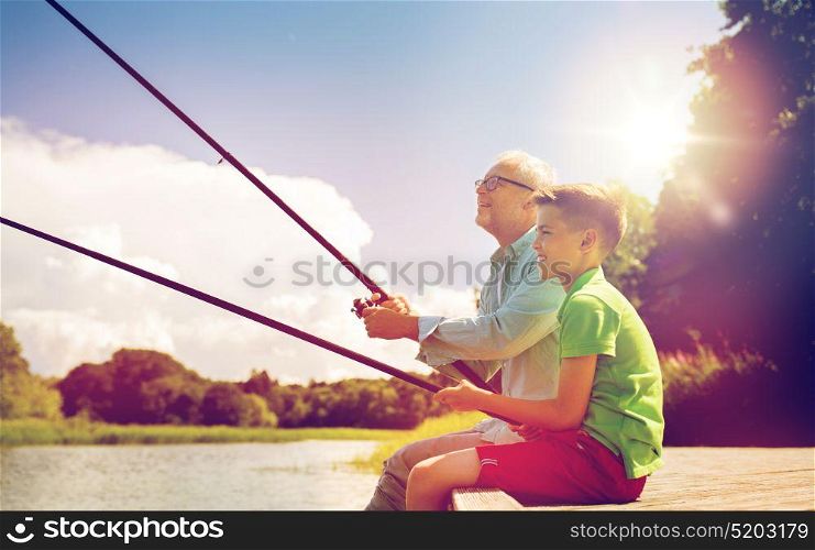 family, generation, summer holidays and people concept - happy grandfather and grandson with fishing rods on river berth. grandfather and grandson fishing on river berth