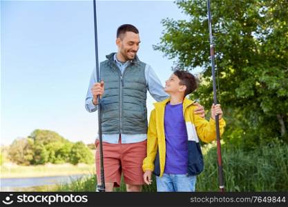 family, generation, summer holidays and people concept - happy smiling father and son with fishing rods on river. happy smiling father and son fishing on river