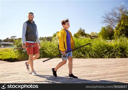 family, generation, summer holidays and people concept - happy smiling father and son with fishing rods on river berth. happy smiling father and son fishing on river
