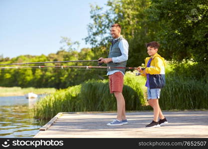 family, generation, summer holidays and people concept - happy smiling father and son with fishing rods on river berth. happy smiling father and son fishing on river