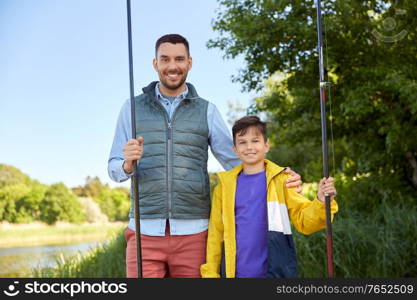 family, generation, summer holidays and people concept - happy smiling father and son with fishing rods on river berth. happy smiling father and son fishing on river