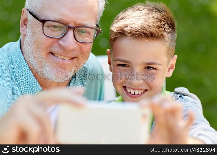 family, generation, technology and people concept - happy grandfather and grandson with smartphone taking selfie at summer park
