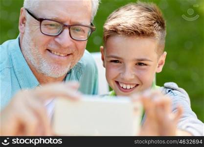 family, generation, technology and people concept - happy grandfather and grandson with smartphone taking selfie at summer park